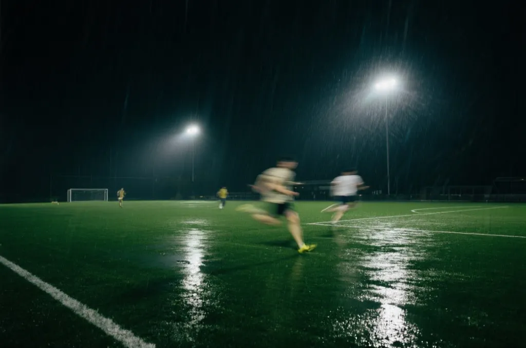 夜间球场在雨后灯光下,草皮湿滑,球员体能消耗明显